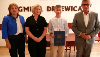 Stypendysta Bartłomiej Kupis z dyplomem i pamiątkową teczką Gminy Drzewica stoi w towarzystwie swojej mamy, Dyrektor ZEAS oraz Burmistrza Drzewicy.