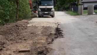 Ciężarówka oraz minikoparka na zwężonym odcinku rozbudowywanej drogi w sąsiedztwie zabudowy mieszkalnej.