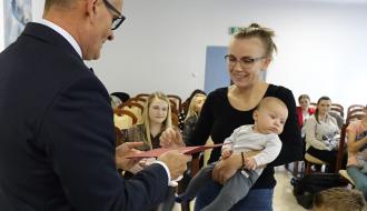 Burmistrz Drzewicy Janusz Reszelewski przekazuje gratulacje mamie trzymającej małe dziecko
