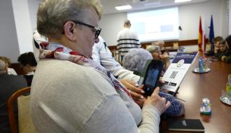 Radna Miejskiej Rady Seniorów Elżbieta Kot za pomocą kodu QR pobiera na smartfon aplikację Movi Guide