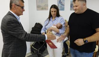 Burmistrz Drzewicy Janusz Reszelewski przekazuje gratulacje rodzicom trzymanego przez mamę małego dziecka