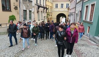 Ponad dwudziestoosobowa grupa z Gminy Drzewica spaceruje brukowaną ulicą Starego Miasta w Lublinie. W tle i po bokach kamienice