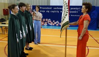 Ceremonia przekazania sztandaru uczniom. Po lewej trzyosobowa reprezentacja uczniów. Po prawej trzymająca sztandar Dyrektor SP w Brzustowcu Barbara Stolarczyk