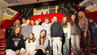 Kilkunastoosobowa grupa uczniów klas siódmych stoi wraz z redaktor Anną Bogusiewicz w studio TV Puls stylizowanym na Festiwal Filmowy w Cannes