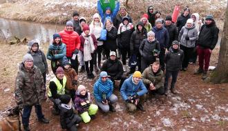 Wspólne zdjęcie kilkudziesięcioosobowej grupy piechurów w lesie na tle rzeki Brzuśni