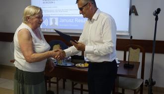 Burmistrz Janusz Reszelewski wręcza oficjalne podziękowania poprzez uścisk dłoni Zofii Danucie Kacprzak – ustępującej sołtys Werówki. W tle widoczny ekran z programem sesji.