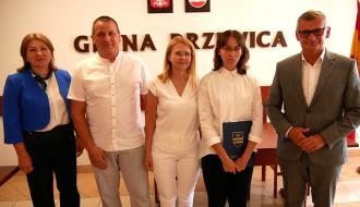 Stypendystka Natalia Wawrzyńczak z dyplomem i pamiątkową teczką Gminy Drzewica stoi w towarzystwie swoich rodziców, Dyrektor ZEAS oraz Burmistrza Drzewicy.