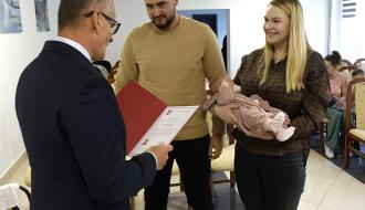 Burmistrz Drzewicy Janusz Reszelewski przekazuje gratulacje rodzicom trzymanego przez mamę małego dziecka
