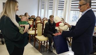 Burmistrz Drzewicy Janusz Reszelewski przekazuje pluszowego misia mamie trzymającej małe dziecko