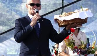 Na scenie do mikrofonu przemawia trzymający bochen chleba Burmistrz Drzewicy Janusz Reszelewski
