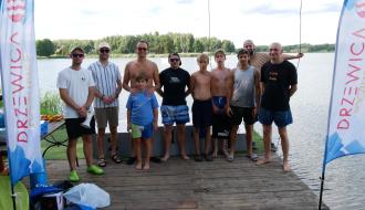 Grupowe zdjęcie dziesięcioosobowej grupy uczestników zawodów wakeboardowych po dekoracji nad brzegiem jeziora