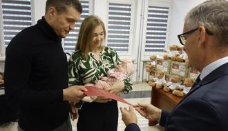 Młoda para trzymająca śpiące niemowlę odbiera czerwoną teczkę okolicznościową z rąk Burmistrza Drzewicy.