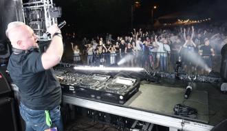 Na scenie za konsolą trzymający mikrofon DJ Omen. W tle bawiąca się publiczność