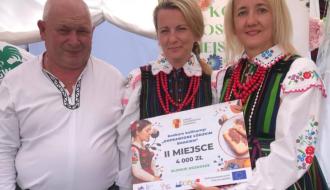 Trzyosobowa reprezentacja KGW Idzikowice w strojach opoczyńskich – jeden pan i dwie panie trzymające promesę z nagrodą za drugie miejsce zajęte podczas Dożynek Województwa Łódzkiego
