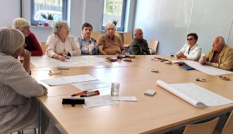 Seniorzy zebrani przy dużym stole konferencyjnym w pomieszczeniu RCK w Drzewicy, pracujący z arkuszami papieru i materiałami szkoleniowymi. 