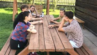 Pięcioosobowa grupa uczestników projektu rozmawia siedząc przy stole na placu obok ośrodka wypoczynkowego
