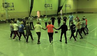 Uczestnicy projektu tańczą w kręgu w hali sportowej
