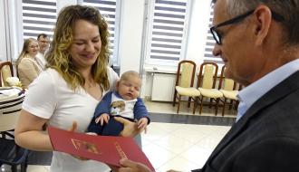 Burmistrz Drzewicy Janusz Reszelewski przekazuje dyplom mamie małego dziecka. Kobieta trzyma bobasa na rękach