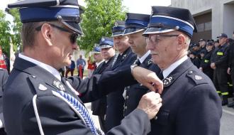 Burmistrz Drzewicy Janusz Reszelewski dekoruje druha Artura Wijatę złotym medalem „Za zasługi dla pożarnictwa”. Obok czterech innych druhów, którym przyznano medale „Za zasługi dla pożarnictwa”