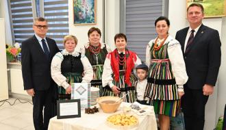 Pięcioosobowa reprezentacja Stowarzyszenia „Moje Tradycje i Innowacje” w Żardkach prezentuje potrawę regionalną przy asyście stojących po bokach Burmistrza Drzewicy Janusza Reszelewskiego i Członka Zarządu Województwa Łódzkiego Artura Bagieńskiego