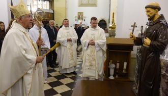 Arcybiskup Wacław Depo trzymający pastorał i kropidło święci figurę świętego Franciszka z Asyżu umieszczoną we wnętrzu kościoła. Obok niego stoją inni kapłani i ministranci w komżach.