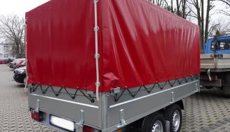 Na parkingu stoi nowa przyczepa z bordową plandeką