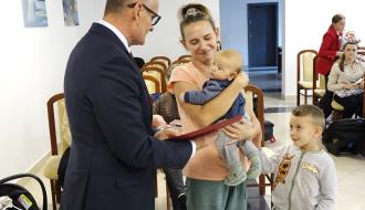 Burmistrz Drzewicy Janusz Reszelewski przekazuje gratulacje mamie trzymającej małe dziecko. Obok starszy syn mamy