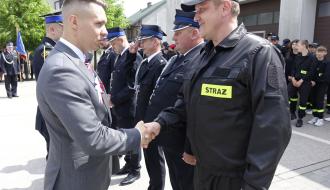 Dyrektor Konrad Gwóźdź gratuluje druhowi Jarosławowi Kasickiemu otrzymania odznaki „Wzorowy Strażak”. Obok pozostali strażacy wyróżnieni odznaką
