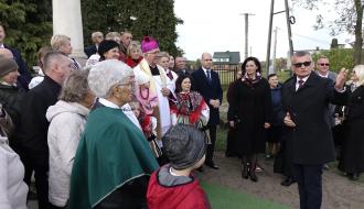 Grupa mieszkańców zgromadzona wokół odrestaurowanej Kolumny Toskańskiej. Burmistrz Drzewicy w ciemnym płaszczu i okularach gestykuluje, zwracając się do zgromadzonych, wśród których są osoby w strojach ludowych oraz Arcybiskup Wacław Depo.