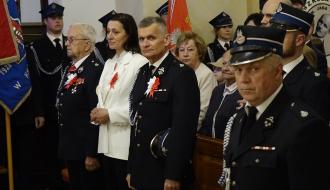 Grupa osób, w tym umundurowani strażacy oraz uczestnicy uroczystości, stoi w kościele pw. św. Łukasza w Drzewicy. Na pierwszym planie widoczni są strażacy w galowych mundurach, w tym Burmistrz Drzewicy,  a także Przewodnicząca Rady Miejskiej w Drzewicy. Wszyscy z biało-czerwonymi kotylionami. W tle sztandary i pozostali uczestnicy mszy.