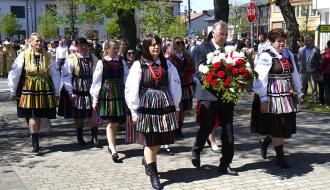 W parku na Placu Wolności ceremonia składania wieńca przez delegację KGW. Idzie kilka pań ubranych w stroje opoczyńskie oraz mężczyzna w garniturze, trzymający wieniec.