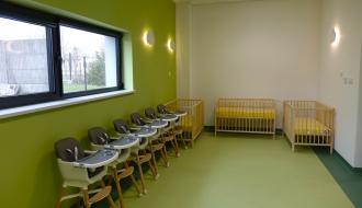 W pokoju znajdują się rzędy nowoczesnych, bezpiecznych krzesełek do karmienia z drewnianymi nóżkami oraz jasne, drewniane łóżeczka dziecięce z żywo żółtymi materacami.
