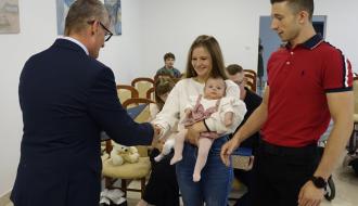 Burmistrz Drzewicy Janusz Reszelewski dyplom mamie małego dziecka. Kobieta trzyma bobasa na rękach. Obok tata malucha.