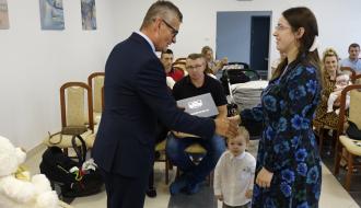 Burmistrz Drzewicy Janusz Reszelewski przekazuje dyplom mamie małego dziecka. Obok starszy brat malucha. 