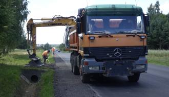 Prace związane z wykonaniem utwardzenia pobocza oraz odtworzenia rowów. Na pierwszym planie koparka podczas pracy.  