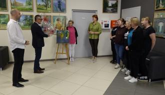 Burmistrz Drzewicy Janusz Reszelewski i Zastępca Burmistrza Dominik Niemirski z życzeniami z okazji Święta Pracownika Kultury w Regionalnym Centrum Kultury w Drzewicy. Osoby znajdują się na holu RCK, burmistrz dzierży kosz słodyczy, obok niego Zastępca. Naprzeciw stoją pracownicy RCK z Dyrektor Aliną Szymańska na czele