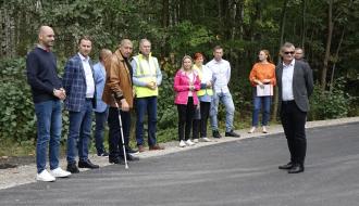 Na wyremontowanej drodze powiatowej stoją uczestnicy odbioru inwestycji – 11 osób. W tle las