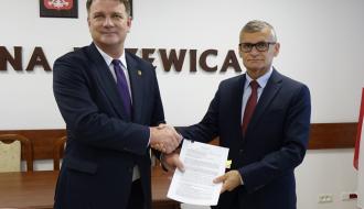 W sali konferencyjnej Urzędu Miejskiego w Drzewicy, przekazują sobie umowę, na tle ściany z napisem Gmina Drzewica, herbem Drzewicy oraz godłem Rzeczpospolitej Polskiej (od lewej) Wice Marszałek Województwa Łódzkiego Artur Bagieński oraz Burmistrz Drzewicy Janusz Reszelewski. 