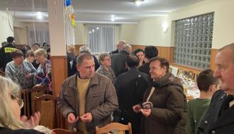 Uczestnicy spotkania łamią się opłatkiem składając życzenia