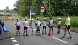 Na tle bogatego drzewostanu oraz zielonych traw przy ul. Stawowej w Drzewicy, na linii startu Drzewica Roller Cup 2025 (od lewej) uczestnicy wyścigu w kat. wiekowej 7-9 lat oraz sędzia techniczny zawodów Waldemar Pęczkowski
