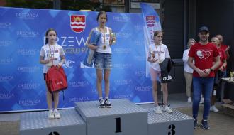Podium w kategorii wiekowej 10-12 lat. W tle błękitna ścianka promocyjna Gminy Drzewica. Od lewej Anna Krzyżanowska, Hanna Gapys, Lena Warchoń oraz Zastępca Burmistrza Drzewicy Dominik Niemirski