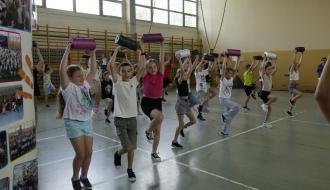 Na zdjęciu uczniowie trzecich klas szkół podstawowych z terenu Gminy Drzewica znajdują się w hali sportowej SP w Drzewicy przy ul. Staszica. Wykonują ćwiczenia praktyczne z rollerami trzymając je nad głową