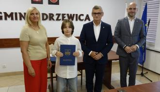 Z rąk Burmistrza Drzewicy Janusza Reszelewskiego stypendium odbiera Marcel Wrzosek. Obok (po lewej) Dyrektor ZEAS w Drzewicy Agnieszka Kwiecień i (po prawej) Zastępca Burmistrza Drzewicy Dominik Niemirski.