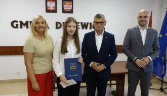 Z rąk Burmistrza Drzewicy Janusza Reszelewskiego stypendium odbiera Julia Wojda. Obok (po lewej) Dyrektor ZEAS w Drzewicy Agnieszka Kwiecień i (po prawej) Zastępca Burmistrza Drzewicy Dominik Niemirski.