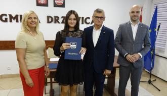 Z rąk Burmistrza Drzewicy Janusza Reszelewskiego stypendium odbiera Michalina Jedynak. Obok (po lewej) Dyrektor ZEAS w Drzewicy Agnieszka Kwiecień i (po prawej) Zastępca Burmistrza Drzewicy Dominik Niemirski.