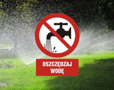 Znak zakazu z kranem oraz napis „OSZCZĘDZAJ WODĘ” na tle zraszanego trawnika.
