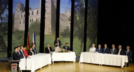 grupa osób siedzących w sali przy stołach z białymi obrusami oraz wielką grafiką w tle przedstawiającą ruiny zamku drzewieckiego, obchodzi ceremonię rocznicy nadania Drzewicy praw miejskich 