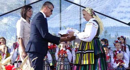 Na scenie Burmistrz Drzewicy Janusz Reszelewski odbiera bochen chleba od dożynkowej starościny Marty Jakubczyk. Obok Burmistrza stoi  Przewodnicząca Rady Miejskiej w Drzewicy Dorota Wiktorowicz