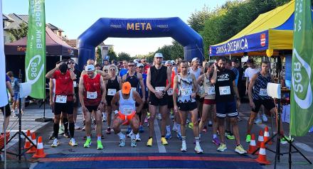 Biegacze w strojach sportowych stoją na linii startu pod niebieską bramą z napisem "META" podczas Drzewica Summer Run.