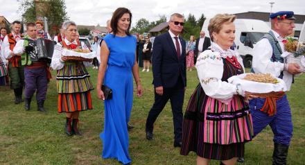 Korowód dożynkowy idący po trawie – na czele osoby w strojach ludowych z chlebami oraz przedstawiciele władz Gminy Drzewica. 